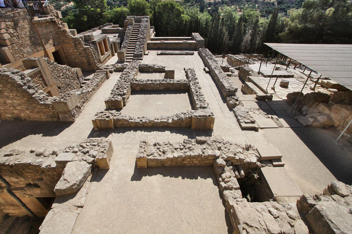 Top view of Knossos ruins showing stone walls, room foundations, and staircases surrounded by greenery.