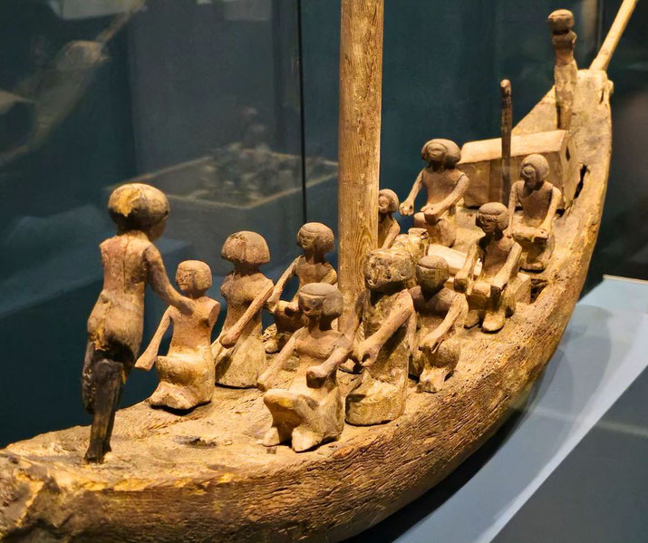 Wooden model of an ancient Egyptian boat with rowers and a helmsman, displayed in a museum.