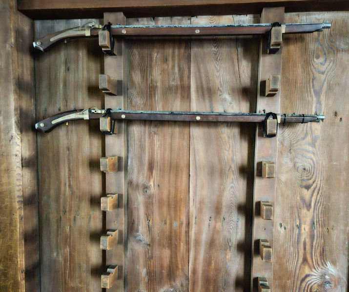 Two antique Japanese matchlock guns (tanegashima) are mounted on a wooden rack against a rustic wooden wall.