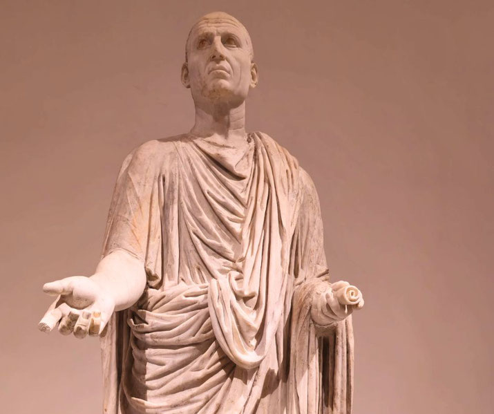Marble statue of a Roman man in a toga, one hand extended and the other holding a scroll, with a solemn, expressive face.