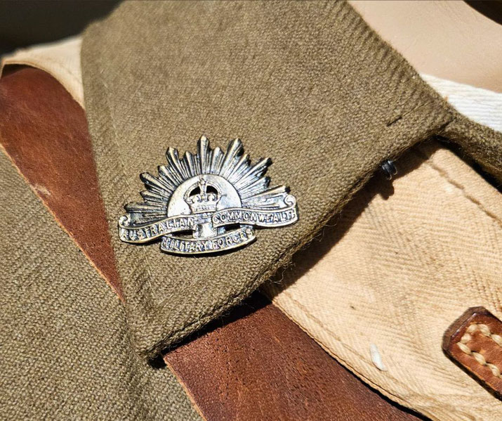 A close-up of an Australian Commonwealth Military Forces badge pinned to a khaki uniform collar.