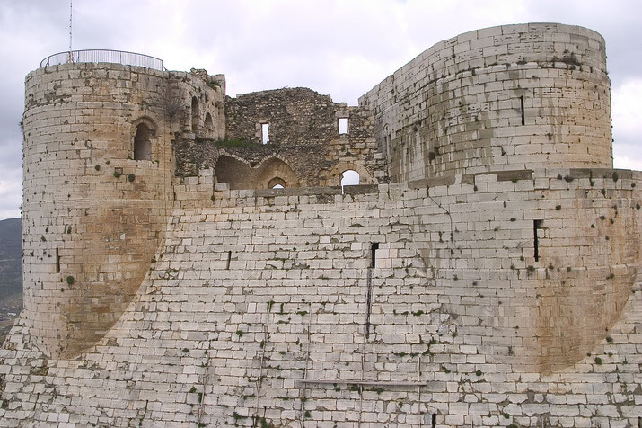 A close-up of the stone walls and towers of Krak des Chevaliers, highlighting the weathered, layered stone construction.