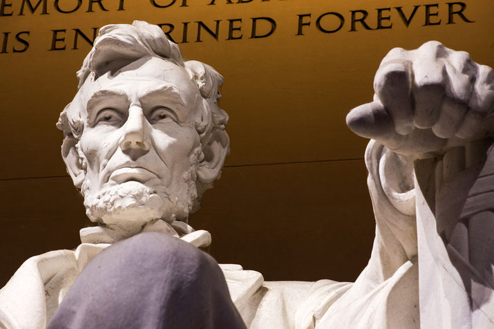Close-up view of the Lincoln Memorial statue, focusing on Abraham Lincoln’s face and clenched hand with partial inscription above.