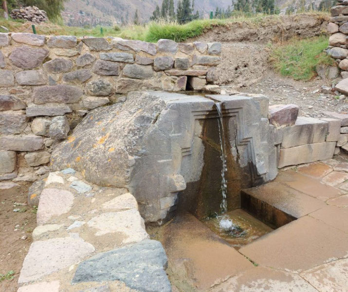 An ancient Inca water fountain at Ollantaytambo, Peru, with precisely carved stonework guiding a small stream of water into a basin. 