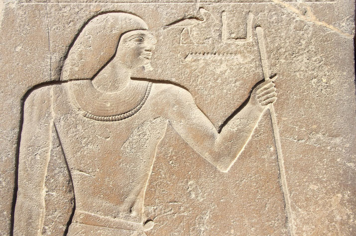 An ancient Egyptian stone relief depicting a noble figure holding a staff. The carving includes hieroglyphs and intricate details, showcasing traditional Egyptian artistic style and symbolism.