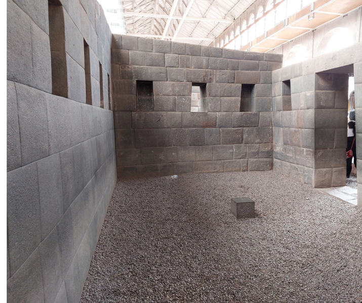 An ancient Inca stone structure features precisely cut dark stone walls with trapezoidal niches and doorways.