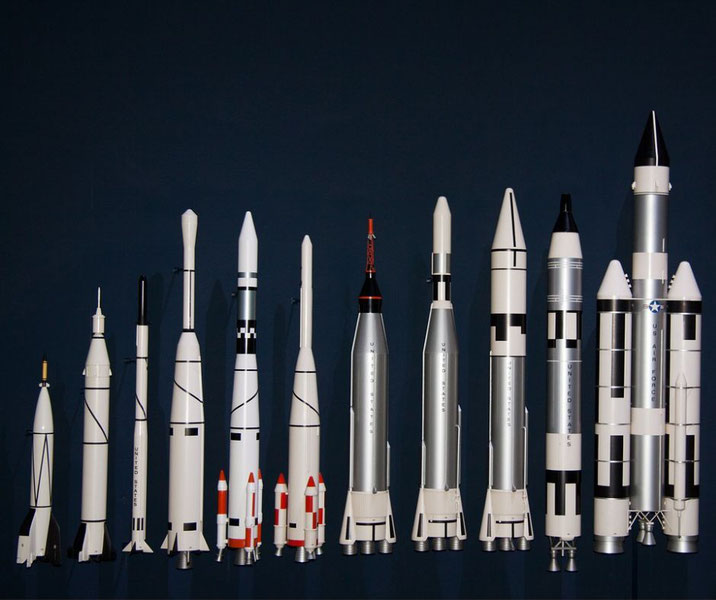 A lineup of various scale model rockets is arranged from shortest to tallest against a dark background.