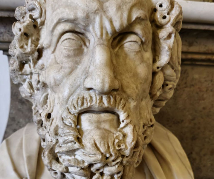 Marble bust of a bearded man with deeply carved curly hair and blind eyes, possibly depicting the ancient Greek poet Homer.
