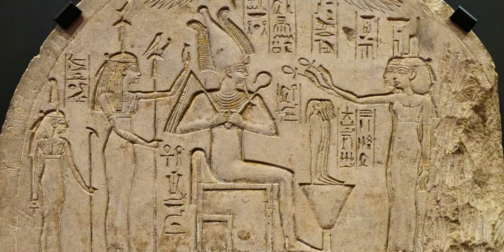 Ancient Egyptian stone relief depicting a seated deity receiving offerings from standing figures, surrounded by hieroglyphs.