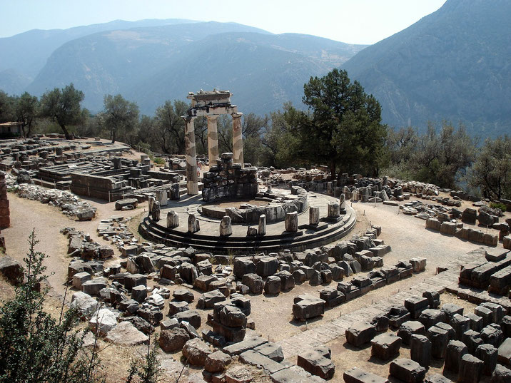 The ruins of the Tholos of Delphi in Greece, featuring three standing columns amid scattered stones.