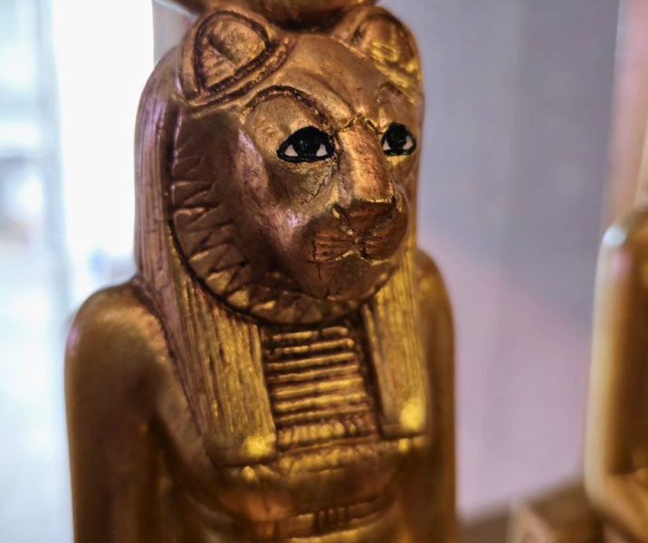 Close-up of a golden statue with a lioness head, representing an ancient Egyptian deity, likely Sekhmet.