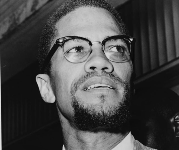 A black-and-white photograph features a close-up of a man with glasses and a beard, looking slightly upward with a determined expression.