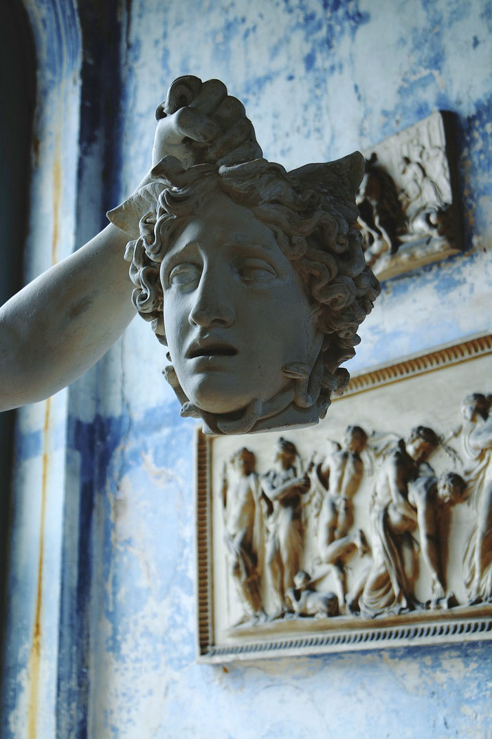 Close-up of a statue showing the severed head of Medusa held aloft, with relief sculptures in the background.
