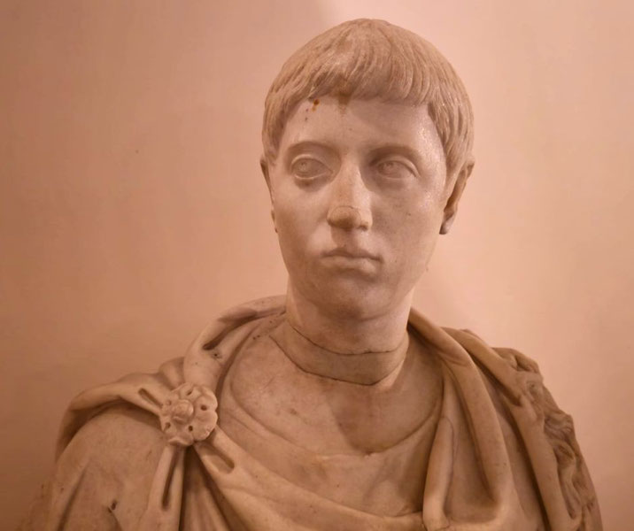 Marble bust of a young man with short hair, wearing a toga fastened with a rosette brooch, gazing slightly to the side with a serious expression.