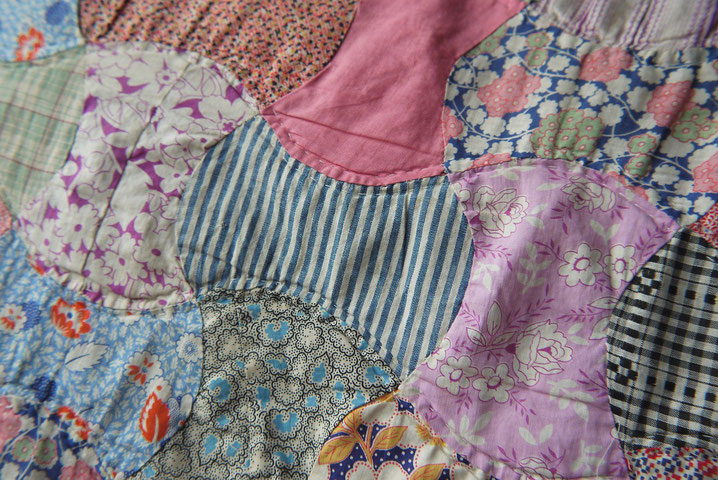 Close-up of a handmade patchwork quilt featuring various floral, striped, and checkered fabric patterns in bright colors.
