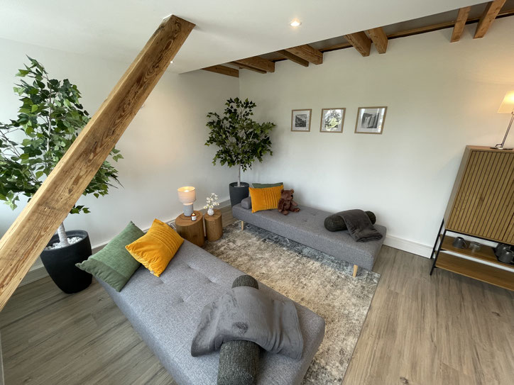 Ruheoase in Lübeck: Auf dem Bild ist eine Lampe und ein kleiner Blumenstrauß in einer Vase zu sehen. Zudem sind zwei gemütlich dekorierte Liegen zu sehen. Es herrscht eine harmonische Stimmung zur Entspannung. Sie hilft beim Abbau von Stress.