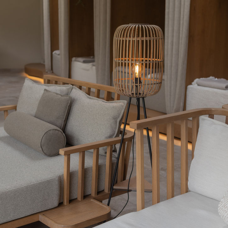 Gemütlicher Spa-Loungebereich mit hellen Polstermöbeln aus Holz, dekorativen Kissen und einer warm leuchtenden Stehlampe im natürlichen Design.