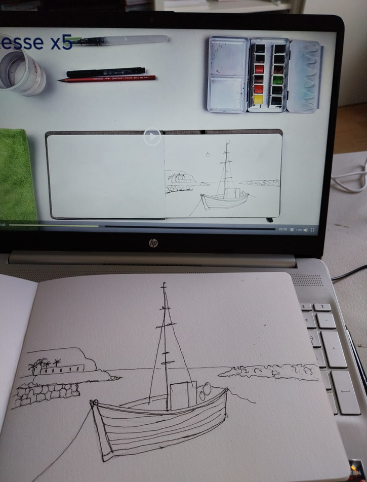Un ordinateur portable affiche un tutoriel de croquis de bateau. Un carnet sur le clavier reproduit ce dessin. Des aquarelles, un pinceau, un crayon et un récipient sont disposés à côté