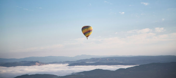 bunter Ballon schwebt über den Wolken im Himmel als Synonym für Freiheit, Möglichkeiten und Chancen.