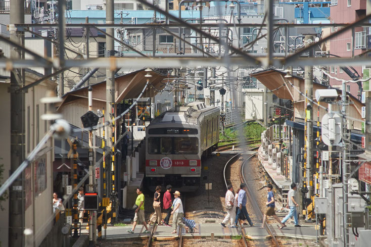 戸越銀座駅に停まる7700系の電車と踏切を渡る人たち