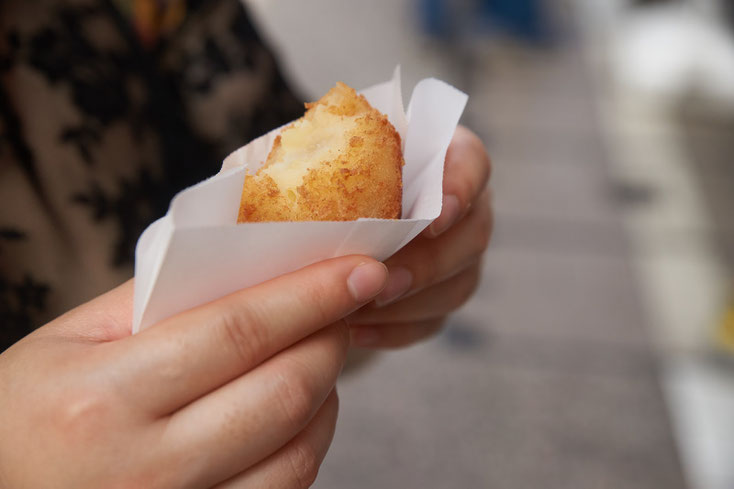 紙に包まれた揚げ物を持つ手。一口かじってある。