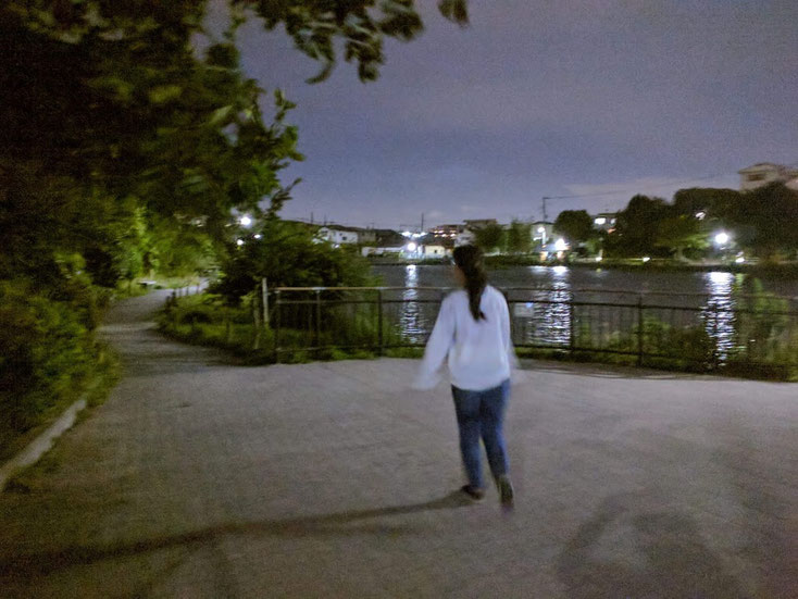 池の遊歩道を走っていく白い服、ジーンズの髪の長い女性サダコさん