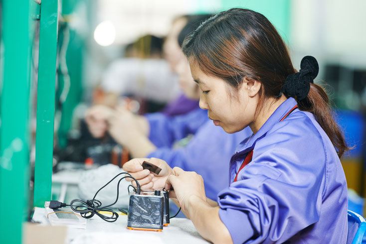 Asiatische Frau arbeitet in einer Manufaktur an einem elektronischen Gerät; Kurtz Detektei Nürnberg