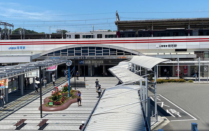 正面から見た明石駅。１階には駅への入り口はファストフードの店舗などが見えます。２階にホームがあり電車が止まっています。