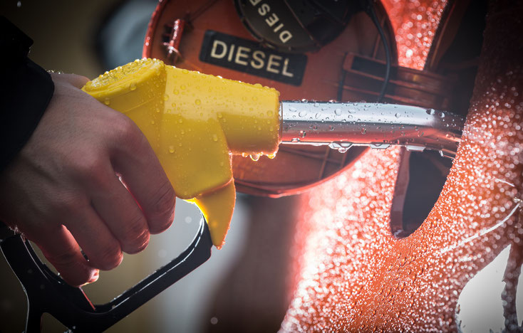 Männliche Hand hält Einfüllstutzen und betankt ein rotes Fahrzeug mit Diesel-Treibstoff; Kurtz Detektei Hamburg.