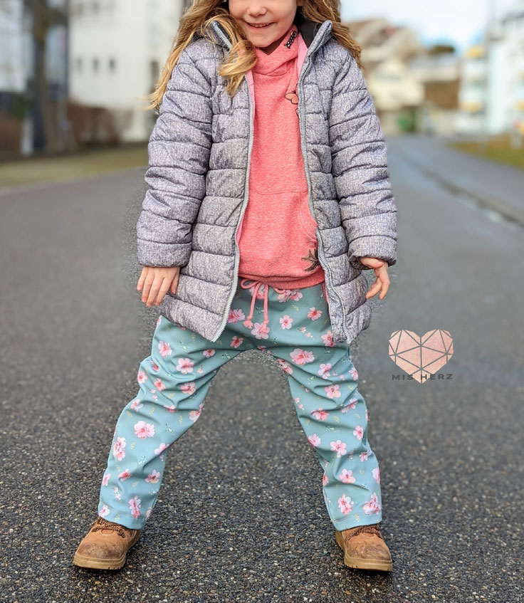 Kind in grauer Pufferjacke, pinkem Hoodie und blau-rosa bedruckter Hibiskus-Outdoorhose - Outdoor Kids Kollektion | Scherzinger-Baby