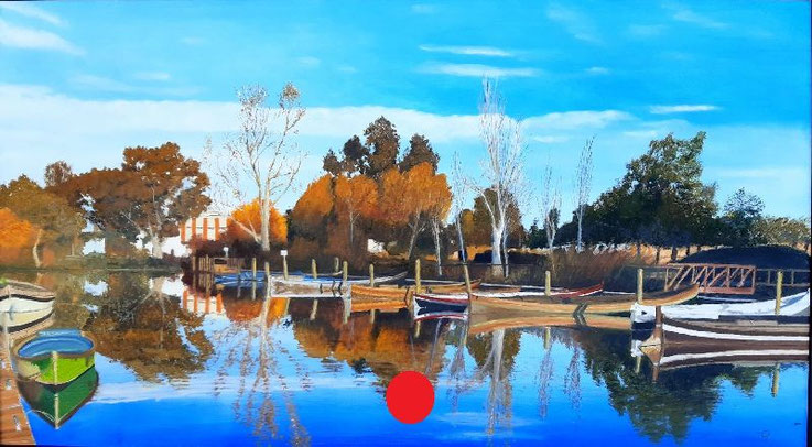 Barcas en el puerto de Catarroja con reflejos en el agua, árboles otoñales y el edificio de La Primitiva al fondo.