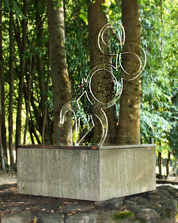 Paolo Grassi sculpture 2508 in transparent plexiglass, installed in wooded landscape on stone and concrete pedestal, conceptual numeric art