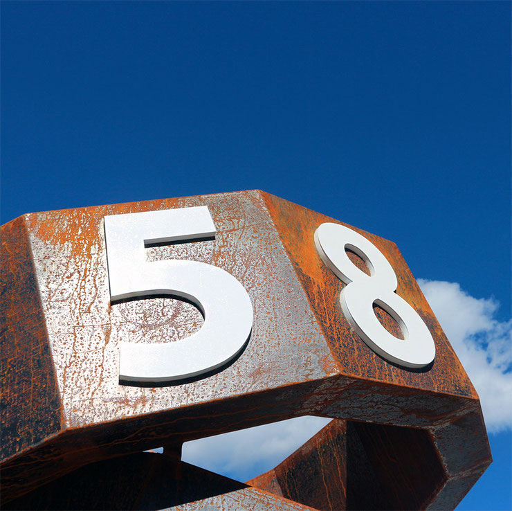 Close-up of Paolo Grassi’s sculpture Thiago with numbers 5 and 8 – blue sky background, corten steel, Lumino, Ticino.