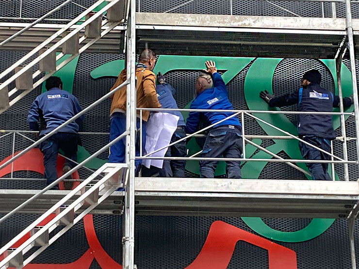 Installation team mounting Paolo Grassi’s “Fortis” in Bellinzona, aligning green numbers on the facade.
