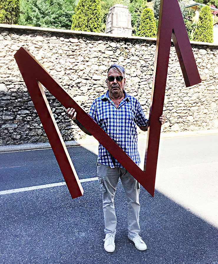 Artist Paolo Grassi holding a large red sculptural letter from his VCMLXXV installation in Locarno.