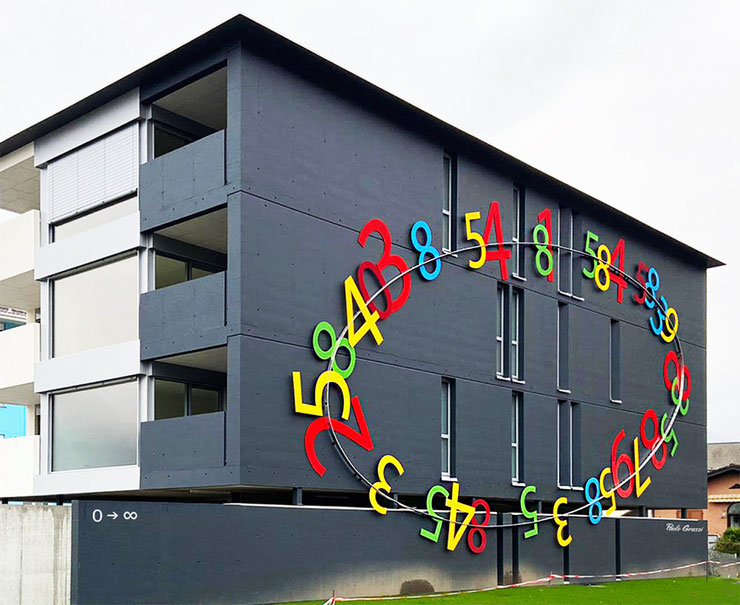 Les Deux Roses by Paolo Grassi curves along the side facade with a stream of vibrant numbers – Les Deux Roses di Paolo Grassi si sviluppa sulla parete laterale con un flusso di numeri vivaci.
