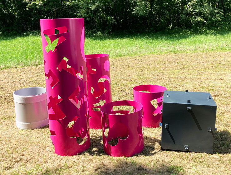 Sculpture parts in magenta, silver, and anthracite tones arranged on the ground before final assembly.