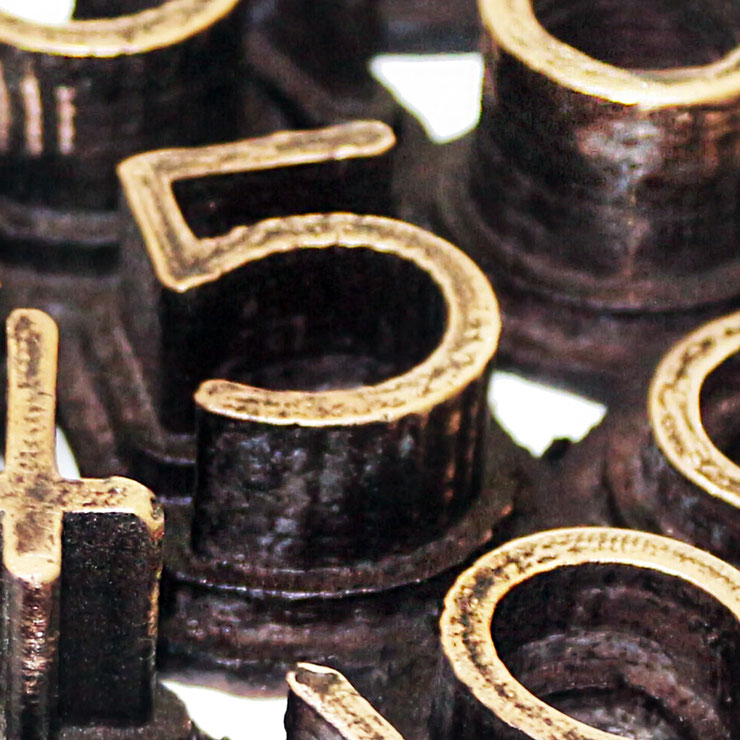 Detail of the bronze sculpture "Nerone" with brown patina, conceptual artwork by Paolo Grassi showing polished numerical elements in relief