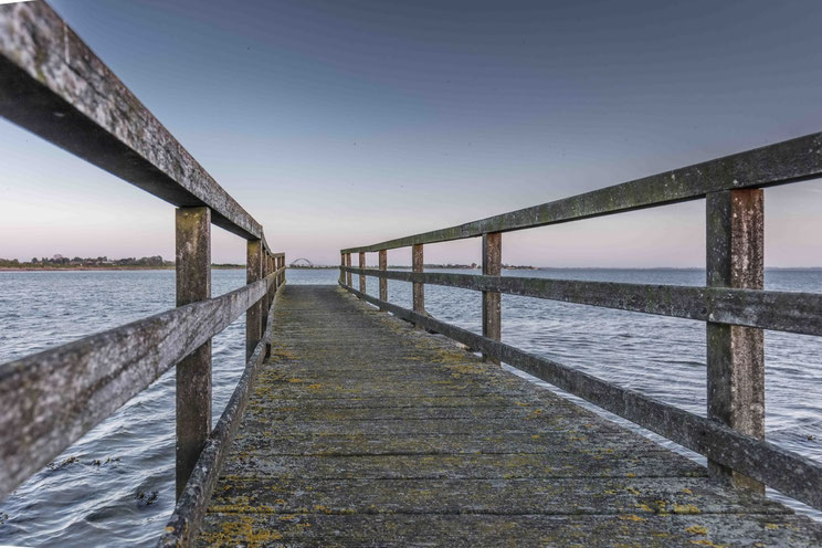 Menschenleerer Steg an der Ostsee mit Blick auf die Fehmarnsund-Brücke: Im Winterurlaub auf Fehmarn sich Zeit nehmen und entschleunigen.