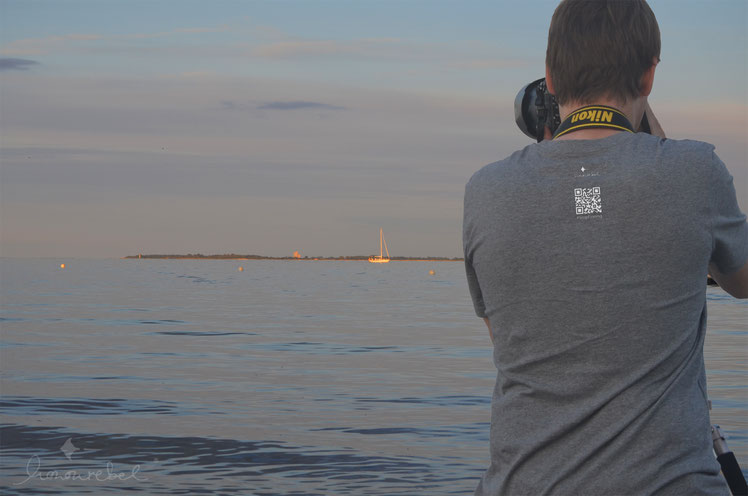 Mann mit Männer STOP FINNING T-Shirt aus Biobaumwolle am Strand von Kiel. Vorne mit Hai, hinten mit QR Code in Grau Weiß.