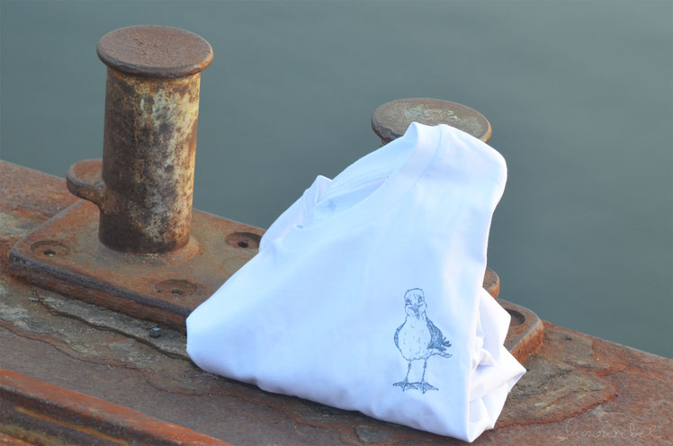 honourebel Slow Fashion. Hochwertiges, weiches T-shirt aus 100 % Biobaumwolle, weiss mit kleiner , lächelnder Kieler Möwe bei Sonnenuntergang am Segelhafen. 
