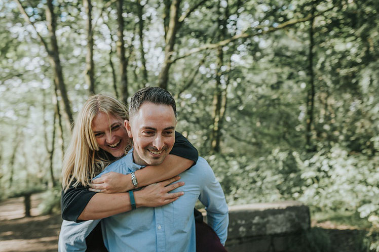 A man giving his fiancee a piggy back ride in the woods