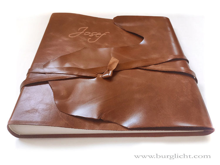 Lederfotoalbum, Rindsleder hellcognac gewachst, Softcover, Überschlag mit natürlichem Abriss und umlaufenden Lederband-Verschluss, Gravur Name, 30cm x 30cm, 100 Seiten naturweiß.