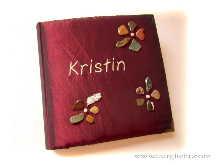 Fotoalbum Feuer & Stein, 30x30cm, 100 Seiten, Bezugstoff changierender Crashtaft dunkelrot, Name gestickt, antikmessingfarbene Buchecken aus Metall, Buchschmuck: Blumen aus lackierten Steinen.