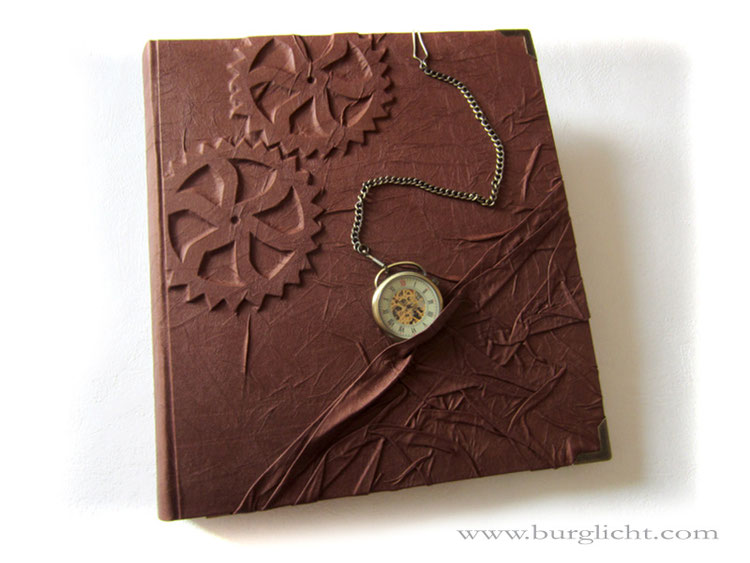 Fotoalbum "Zeitreise", Hardcover-Bucheinband mit Flachrelief Zahnräder, Stoffbezug rotbraun, mechanische Taschenuhr, Metall-Buchecken, 30cm x 33cm Hochformat, 100 Seiten weiß, mit Pergaminzwischenblättern.