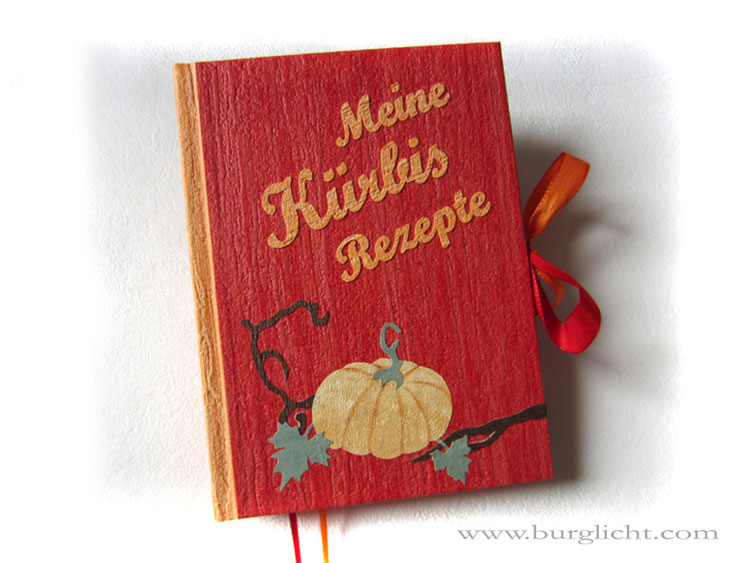 Buch "Meine Kürbis Rezepte", A5 Hardcover-Bucheinband, Schmuck-/Strukturpapier rot orange grün braun, Schleifenverschluss, Buchblocklagen abwechselnd rot und orange, Leseband rot und orange.