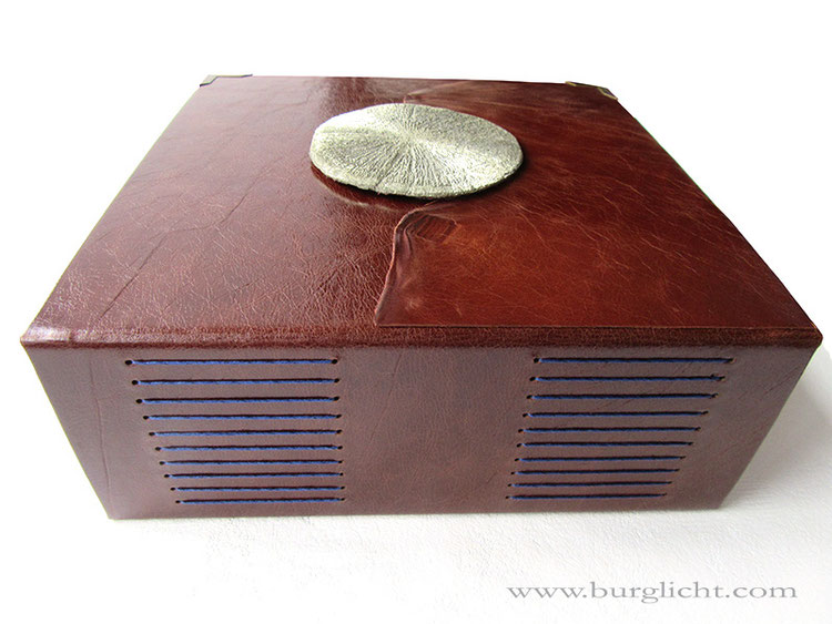 Buch mit Pyritsonne, Hardcover-Ledereinband, Lederfarbe dunkelcognac, Langstichheftung blau, Buchecken messingfarben, 26cm x 26cm, 300 Seiten Zeichenkarton naturweiß. 