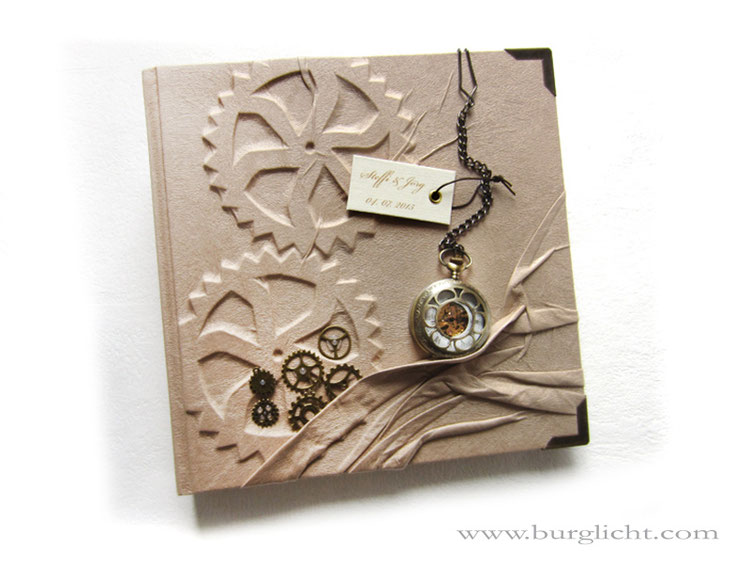 Fotoalbum "Zeitreise", Hardcover-Bucheinband mit Flachrelief Zahnräder, Stoffbezug cremefarben, echte mechanische Taschenuhr, Label bedruckt, Buchecken und Zahnräder messingfarben.