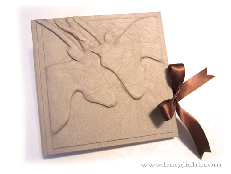 Foto-Gästebuch, Hochrelief Steinbockpaar, 24x24cm, 30 Blatt Fotokarton hellcreme, Stoff antik white pearl, Schleifenverschluss.