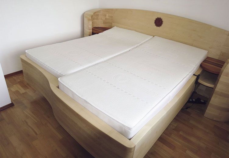 Bett "Passgeneu" aus massivem Ahorn mit einseitig verkürzter Liegefläche, gebogenes Kopfteil mit Sonne und integrierten Ablagen